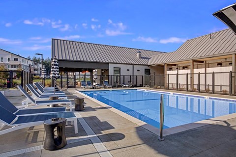 A swimming pool area with sun loungers and a building in the background.