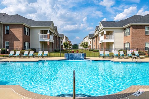 A swimming pool in front of apartment buildings with lounge chairs around it.