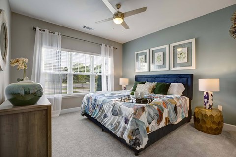A bedroom with a bed, a ceiling fan, and a vase on a wooden stand.