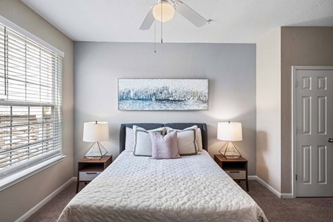 A bedroom with a large bed, two lamps, and a painting on the wall with ample natural light.