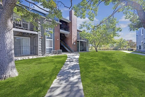 A tree-lined walkway leads to a brick building.