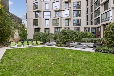A large grassy area in front of a building with a bench and a tree.