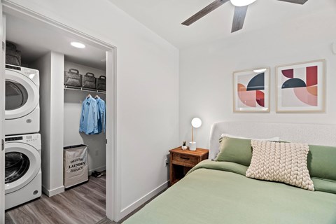 A bedroom with a green bed and a washing machine in the closet.