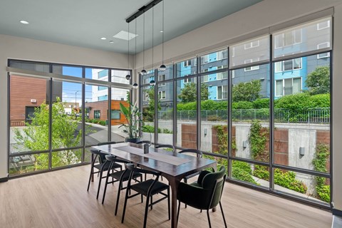 A dining table with chairs is set up in a room with a view of a building and greenery outside.