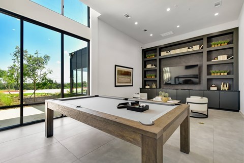 A pool table is in the middle of a room with a view of the outside.