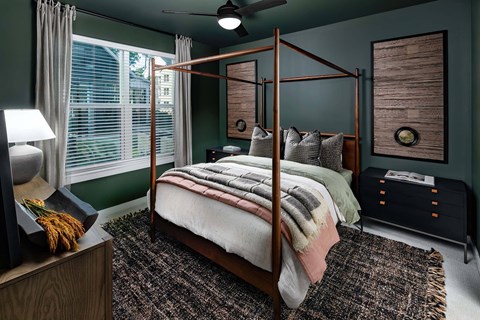 A bedroom with a four-poster bed and a window with white blinds.