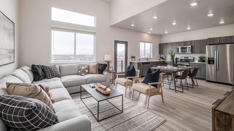 A modern living room with a grey sofa, wooden chairs, and a kitchen in the background.