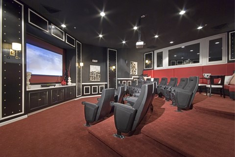 A row of black cinema seats are arranged in front of a large screen.
