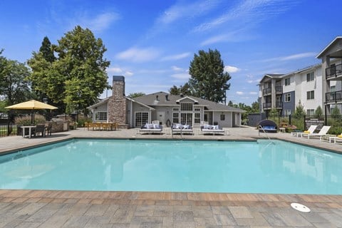 A large swimming pool surrounded by a stone patio and lounge chairs.