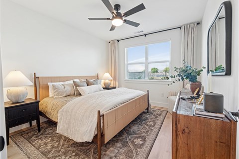 A bedroom with a large bed, a ceiling fan, and a window with a view.
