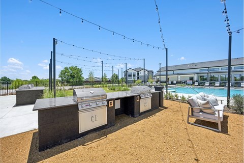 A sunny day at a barbecue area with grills and a pool in the background.