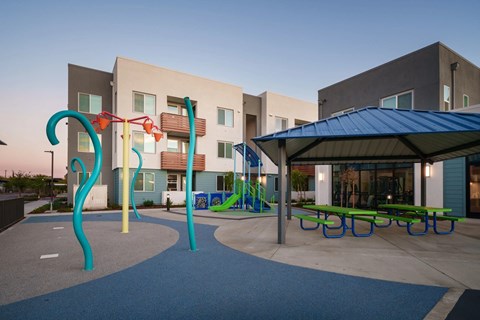 A playground with a blue canopy and a slide in front of a building.