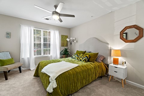 A bedroom with a green bedspread and a white ceiling fan.