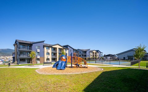 A playground with a slide and swings is in front of apartment buildings.