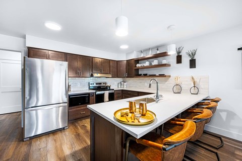 A modern kitchen with a stainless steel refrigerator and wooden chairs.