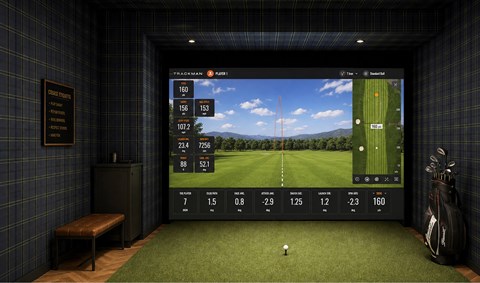 A golf simulator room with a screen showing a golf course and a ball on the ground.