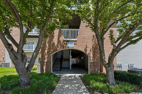 A tree-lined pathway leads to a brick building's arched entrance.