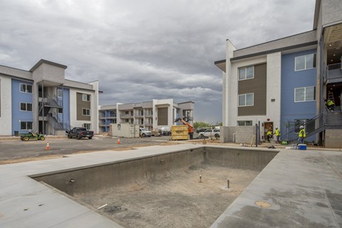 A construction site with a large empty pool in the foreground and several buildings under construction in the background.