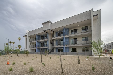 A modern building with blue balconies and a gravel lot in front.