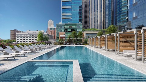 A large swimming pool with lounge chairs and a city skyline in the background.