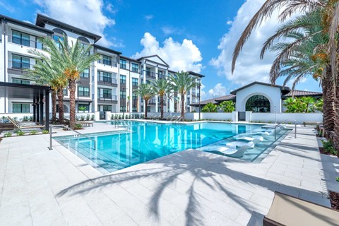 A large swimming pool surrounded by palm trees and a building in the background.