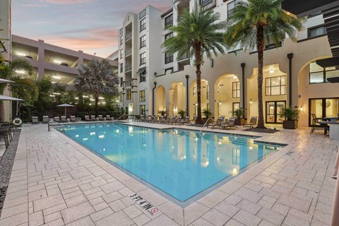 A pool surrounded by a building and palm trees.