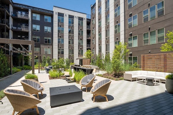 an outdoor lounge area with chairs and tables in front of tall buildings