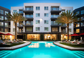 an outdoor pool with lounge chairs and palm trees in front of an apartment building at VORA LUX, California, 92120