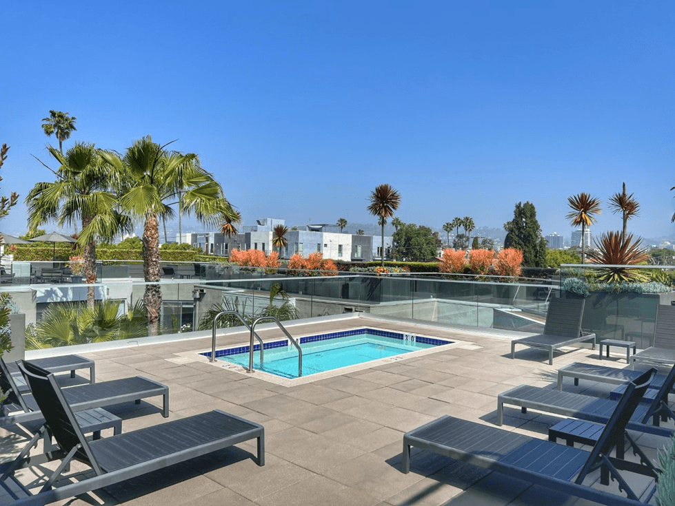 a pool and lounge chairs on a roof with palm trees and houses in the background  at The LC, Los Angeles, CA