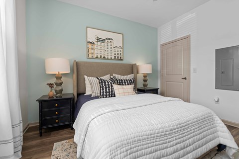 A bedroom with a large bed, two lamps, and a painting on the wall.