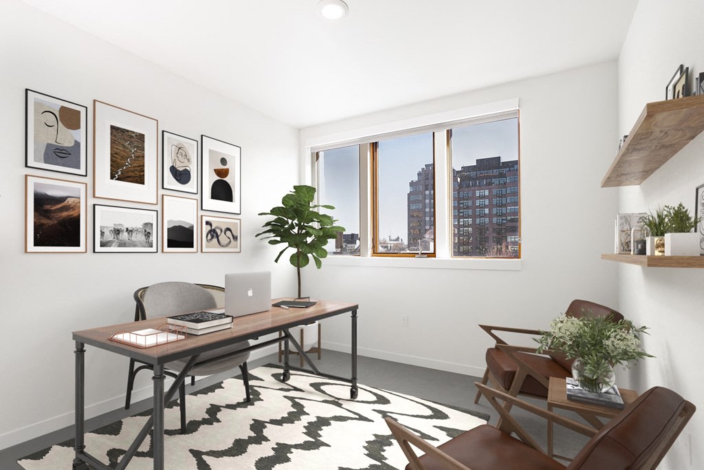a home office with a desk and a window and a wall of framed photos