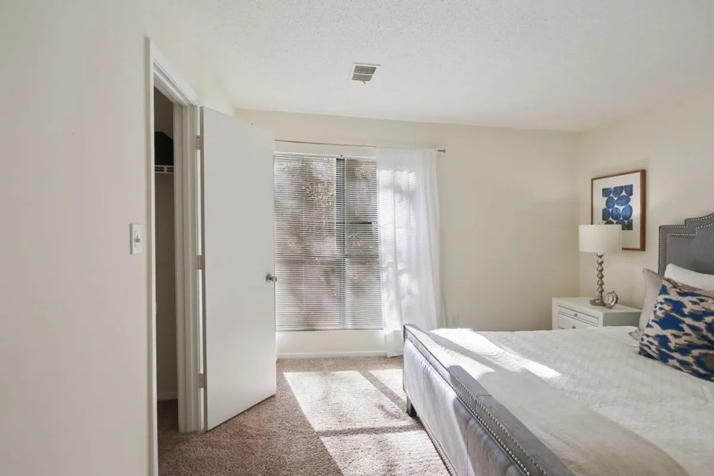 A bedroom with a bed, a nightstand, and a window with blinds.