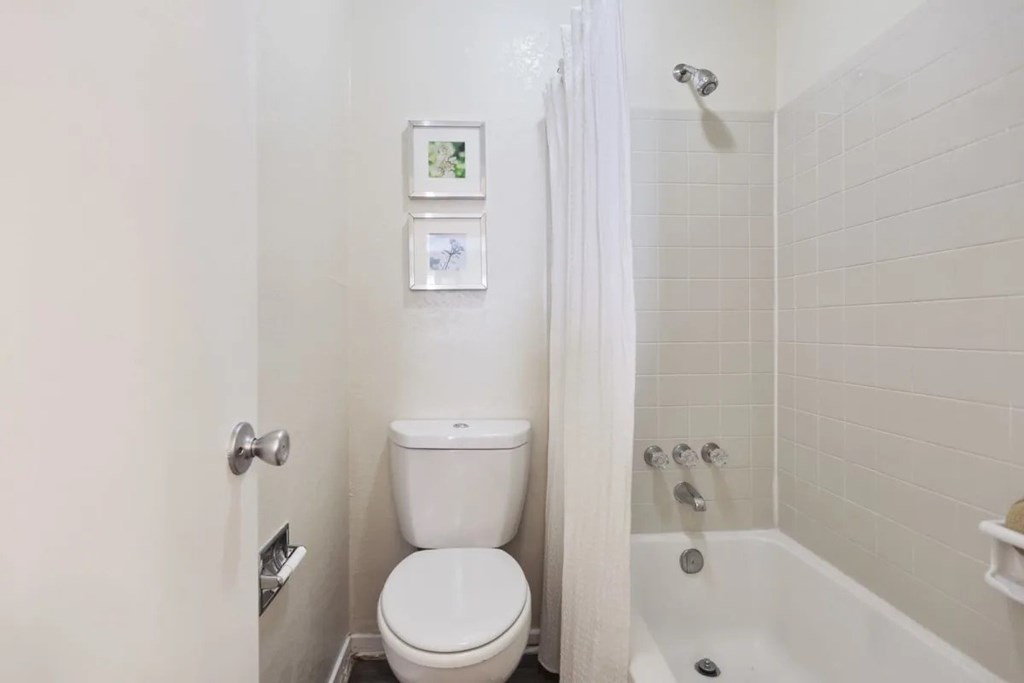 A white toilet sits in a bathroom next to a white bathtub.