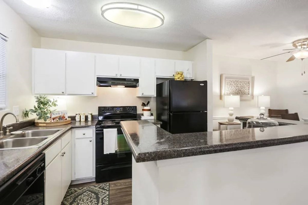 A black refrigerator is in a kitchen with white cabinets.