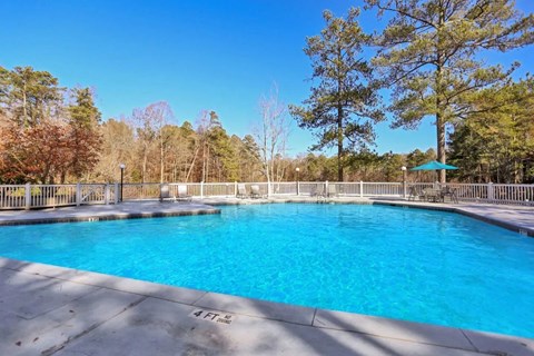 A large swimming pool surrounded by a white fence and trees.
