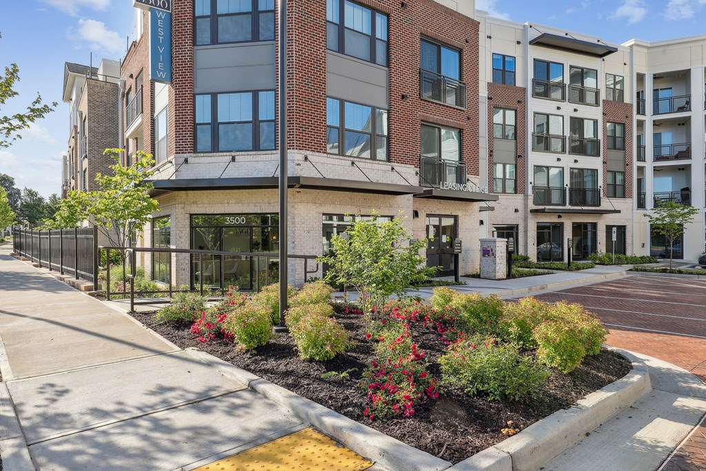 an apartment building with a sidewalk and landscaping in front of it