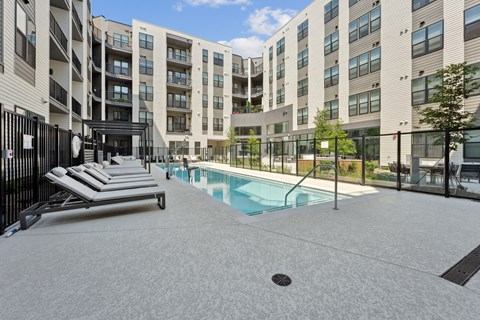 A pool area with sun loungers and a building in the background.