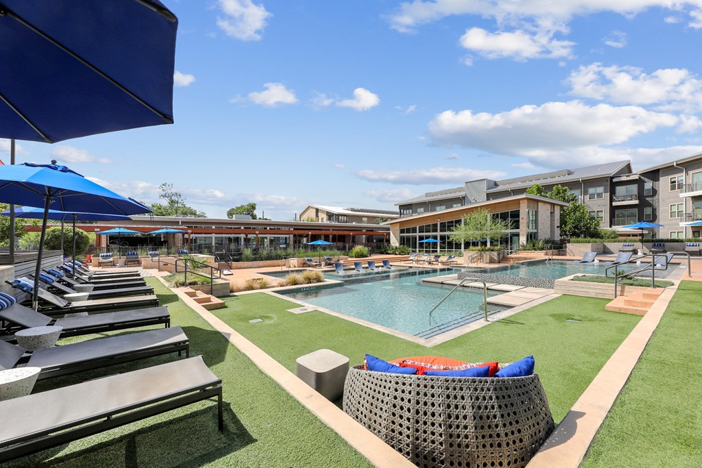 A sunny day at the poolside with blue umbrellas and loungers.
