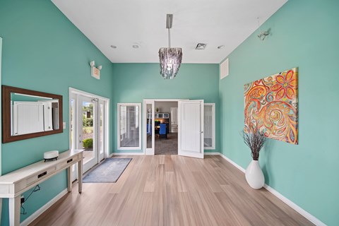 A hallway with a chandelier, a mirror, and a vase on the floor.