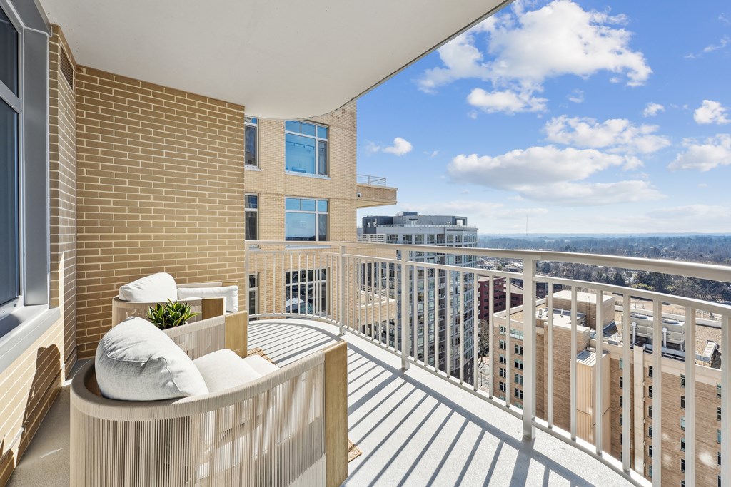 A balcony with a couch and pillows overlooks a cityscape.