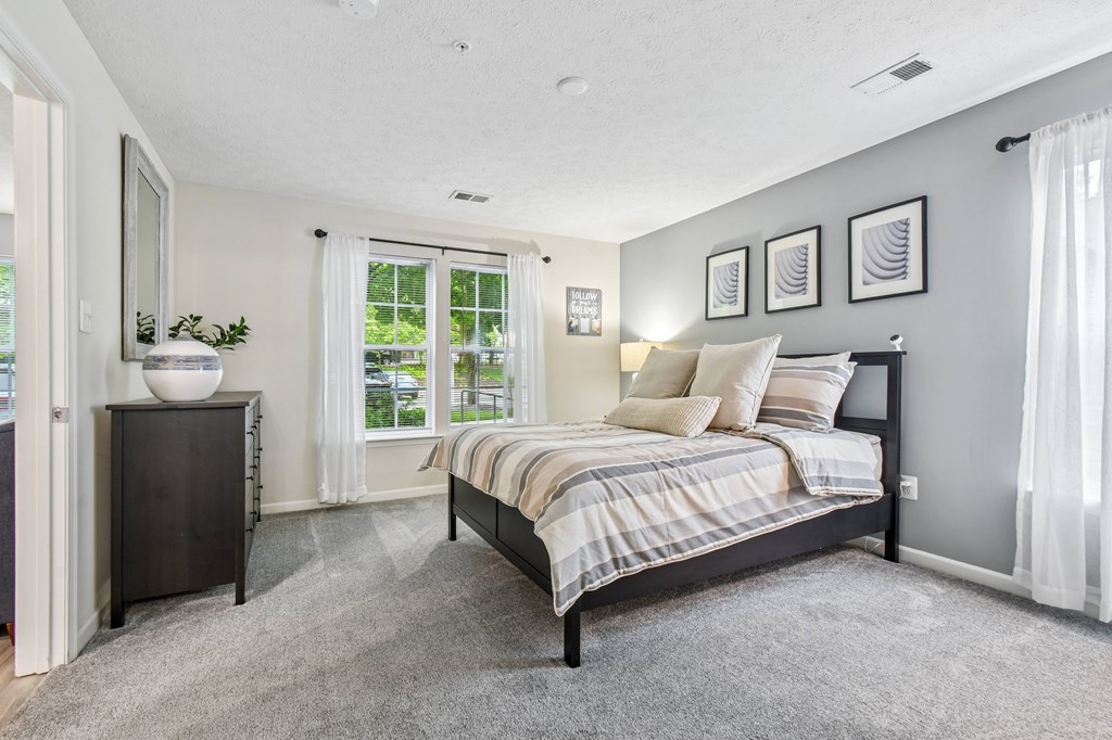 A bedroom with a bed, nightstand, and a window with curtains.