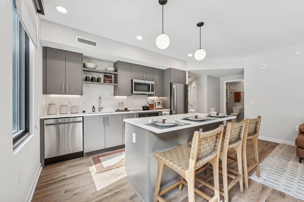 A modern kitchen with wooden chairs and stainless steel appliances.
