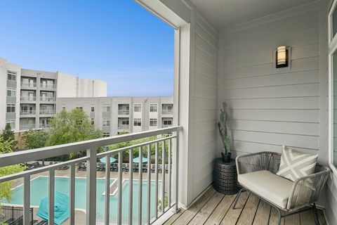 A balcony with a chair and a potted plant overlooks a pool and apartment building.