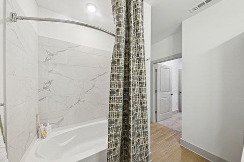 A bathroom with a marble patterned tub and a shower curtain.