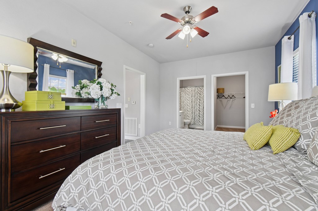 A bedroom with a patterned bedspread and a ceiling fan.
