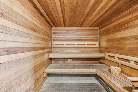 A wooden sauna with benches and a bucket on the floor.