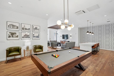A pool table is in the middle of a room with a green chair and pictures on the wall.