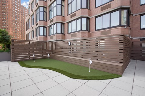 a wooden fence around a putting green in front of a brick building