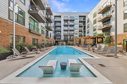 A large outdoor swimming pool surrounded by lounge chairs and buildings.