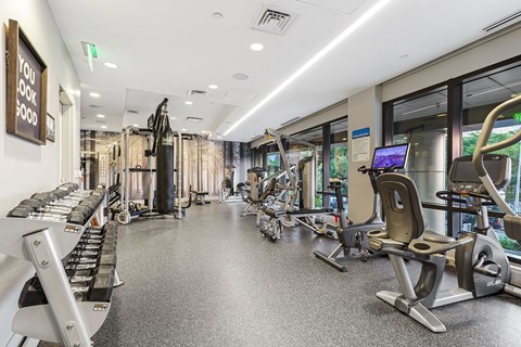 a gym with cardio equipment and weights in a building with windows